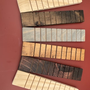 May include: Six wooden blocks with different stain colors. The blocks are all the same size and shape, and they have a series of grooves running along their length. The blocks are arranged in a semi-circle, with the lightest block at the bottom and the darkest block at the top.