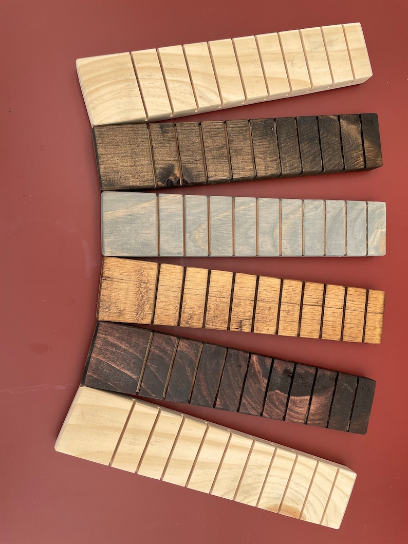 May include: Six wooden blocks with different stain colors. The blocks are all the same size and shape, and they have a series of grooves running along their length. The blocks are arranged in a semi-circle, with the lightest block at the bottom and the darkest block at the top.