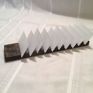 May include: A wooden card holder with a dark brown stain. The holder has eight slots for cards, and the cards are white.