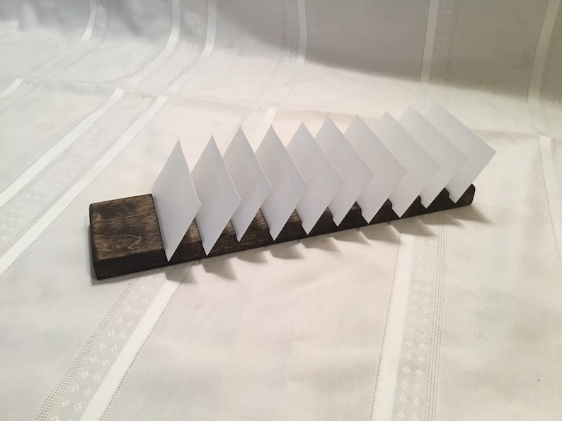 May include: A wooden card holder with a dark brown stain. The holder has eight slots for cards, and the cards are white.