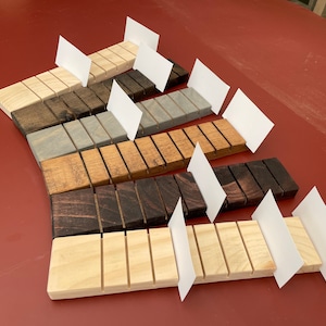 May include: A set of eight wooden business card holders in various wood stains, including natural, light brown, gray, dark brown, and black. Each holder has eight slots for business cards and is displayed with blank white cards.
