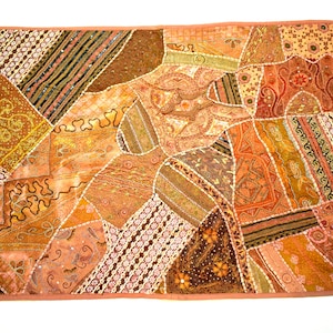 May include: A patchwork wall tapestry featuring a range of brown, orange, and pink fabrics. The tapestry is adorned with sequins and embroidery.