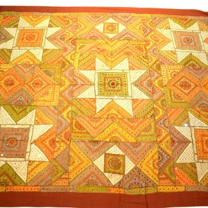 May include: A large, colourful quilt with a patchwork design featuring a variety of geometric shapes and patterns. The quilt is made of different shades of orange, yellow, green, and white fabric. The quilt is decorated with small, reflective mirrors.