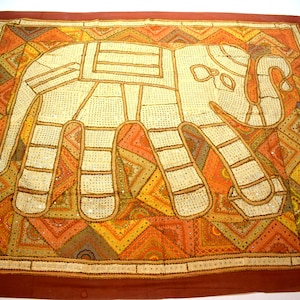 May include: A white elephant embroidered on a tapestry with a patchwork design of orange, yellow, brown, and green geometric shapes.