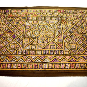 May include: A large, rectangular, brown fabric wall hanging with a colourful geometric pattern. The pattern is made up of squares, triangles, and diamonds in shades of pink, purple, yellow, and blue.