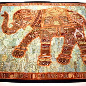 May include: A large tapestry featuring a patchwork elephant design. The elephant is made of various fabrics and colours, including brown, orange, and gold. The tapestry has a black border.
