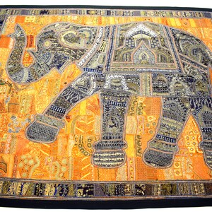 May include: A colourful tapestry featuring an embroidered elephant in shades of blue and gold. The elephant is surrounded by intricate patterns and details, creating a vibrant and textured design.