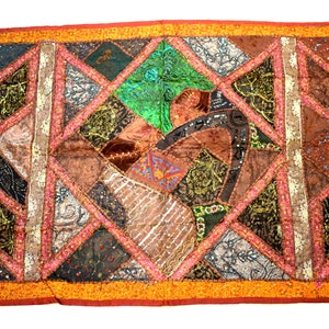May include: A colourful patchwork wall hanging with a geometric design. The fabric is a mix of brown, green, pink, and gold. The hanging is decorated with sequins and embroidery.