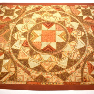 May include: A large, square, brown and cream patchwork quilt with a central circular design. The quilt is decorated with sequins and small mirrors. The central design features a large star shape.