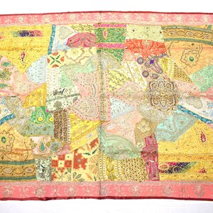May include: A colorful patchwork wall hanging with a pink border and intricate embroidery. The fabric is a mix of different textures and patterns, including paisley, floral, and geometric designs. The wall hanging is adorned with sequins and beads, adding a touch of sparkle.