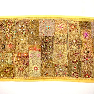 May include: A gold and brown tapestry with a patchwork design. The tapestry is made of different fabrics and is decorated with beads and sequins.