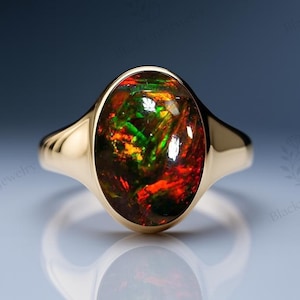 May include: A gold ring with an oval-shaped, multi-colored opal gemstone. The opal displays a vibrant mix of red, green, and yellow hues. The ring's band is a simple, polished gold design.