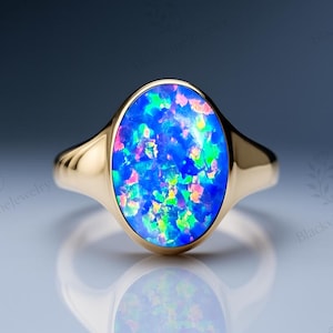 Peut inclure: Une bague en or ornée d'une opale ovale. L'opale présente une couleur de base bleue vibrante avec des éclats de vert, de rose et de jaune. La bague a un anneau en or poli simple.