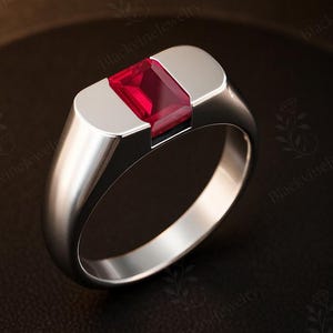 Peut inclure: Une bague en argent avec une pierre précieuse rouge vif de forme rectangulaire. La bague présente un design moderne et minimaliste avec une finition polie. La pierre est sertie dans un sertissage à lunette, et le jonc est lisse et arrondi.