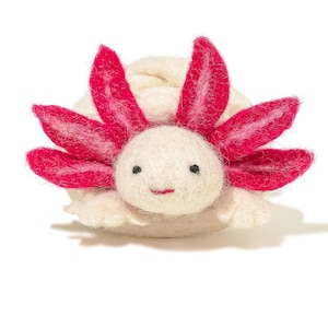 May include: A handmade felt axolotl figurine. The axolotl has a cream-colored body with bright pink gills and a small, smiling mouth. The figurine is made of soft felt and has small black eyes.