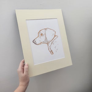 May include: A framed print of a dog's head in a copper foil finish. The dog is a dachshund with floppy ears and a long snout.