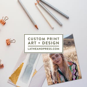 May include: An overhead shot features art supplies and printed art. Pencils, paper clips, and a portrait are arranged on a white surface. The image includes a print with the text "CUSTOM PRINT ART + DESIGN" and the website "LATHEANDPRESS.COM".