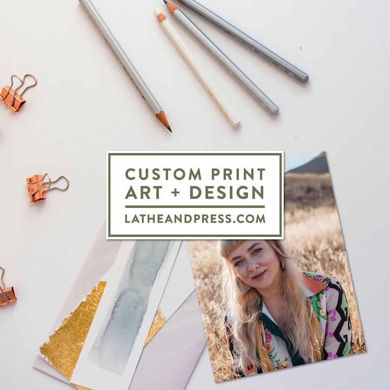 May include: An overhead shot features art supplies and printed art. Pencils, paper clips, and a portrait are arranged on a white surface. The image includes a print with the text "CUSTOM PRINT ART + DESIGN" and the website "LATHEANDPRESS.COM".