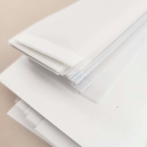 May include: A stack of white paper sheets, with a few sheets slightly separated, creating a layered effect. The paper has a smooth, clean surface, and the edges appear slightly rough. The image is well-lit, highlighting the paper's texture and color.
