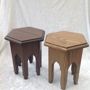 May include: Two wooden hexagonal side tables. One is stained a dark brown, the other a light brown. Both have arched legs and a raised edge around the tabletop. The tables are approximately 46 cm tall.