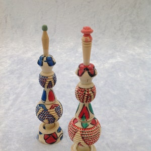Peut inclure: Deux bouchons de bouteille décoratifs en bois avec des motifs peints colorés. Les bouchons sont en forme de sphère avec un sommet pointu et une base. Les motifs présentent des peintures rouge, bleue, verte et blanche.