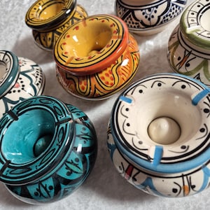 May include: Six ceramic ashtrays with intricate designs. The ashtrays are in various colors, including blue, green, yellow, and white. Each ashtray has a unique pattern and design.