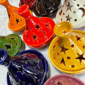May include: A collection of seven ceramic incense burners with star and crescent moon cutouts. The burners are in various colours, including orange, red, black, white, green, blue, and purple.