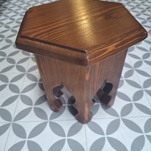 May include: A hexagonal wooden stool with a dark brown stain. The stool has a unique, intricate design on the legs.