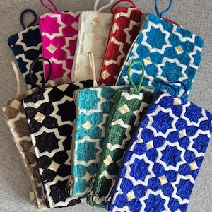 Può includere: Una collezione di pochette rettangolari colorate con un motivo a stella. Le pochette sono in vari colori, tra cui blu, rosa, rosso e verde, con un design a stella bianco o oro a contrasto. Ogni pochette ha una cerniera e un anello.