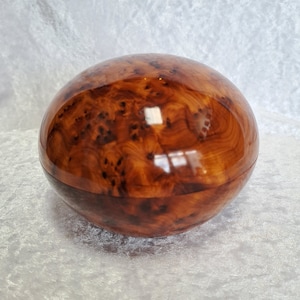 Peut inclure: Une boîte ronde en bois avec un motif de grain de bois naturel et une finition brillante. La boîte est en bois de loupe et présente un motif unique et complexe.