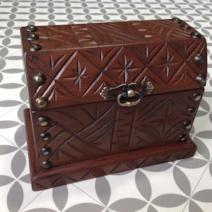 May include: A small wooden box with a carved design and metal accents. The box has a hinged lid and a metal handle. The box is brown and has a distressed finish.