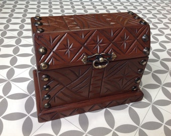 May include: A small wooden box with a carved design and metal accents. The box has a hinged lid and a metal handle. The box is brown and has a distressed finish.