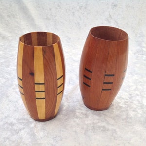 May include: Two wooden vases with different patterns. The vase on the left has a striped pattern with black accents. The vase on the right has a solid wood colour with black lines.