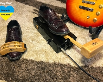 May include: A percussion device featuring a wooden tambourine attachment on a dark burgundy leather brogue shoe and a wooden mallet connected to a black rectangular control box with a cable, alongside a sunburst electric guitar.
