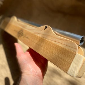May include: A wooden box with a metal tube inside. The box is made of light wood and has a natural finish. The tube is silver and has a rounded end.
