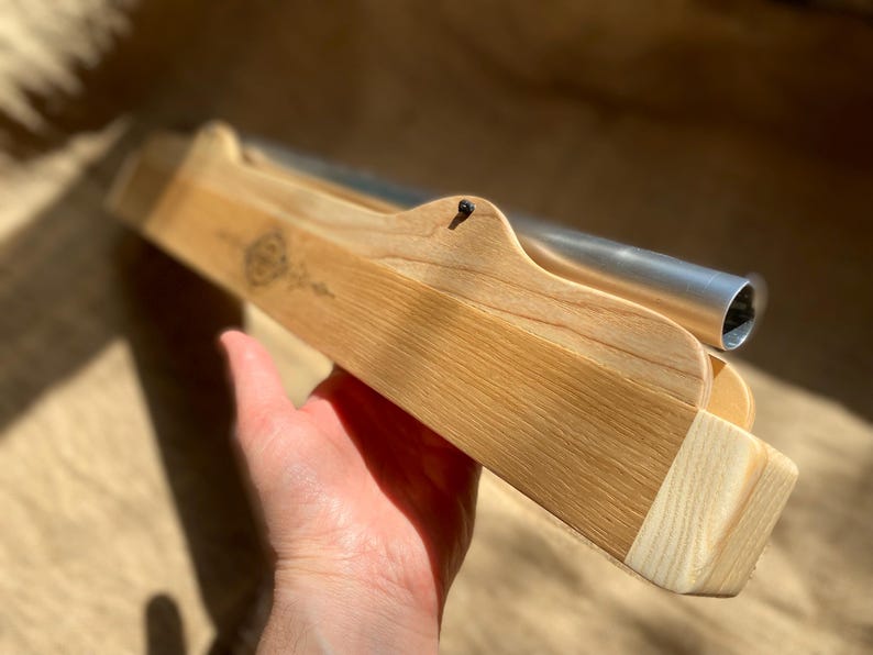 May include: A wooden box with a metal tube inside. The box is made of light wood and has a natural finish. The tube is silver and has a rounded end.