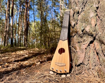 May include: A light-colored wooden stringed instrument with a triangular body, a circular sound hole, and a dark fretboard. The instrument features four metal strings anchored at the base with silver tuning pegs and rests against a tree trunk.