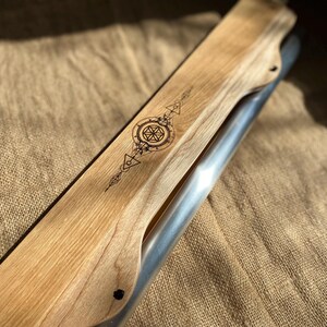 May include: A wooden and metal musical instrument with a geometric design burned into the wood. The instrument is resting on a burlap surface.