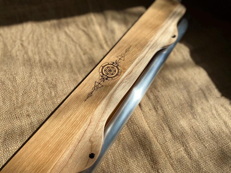 May include: A wooden and metal musical instrument with a geometric design burned into the wood. The instrument is resting on a burlap surface.