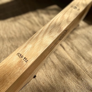 May include: A wooden tuning fork with the inscription "639 Hz" on the side. The tuning fork is resting on a brown fabric surface.