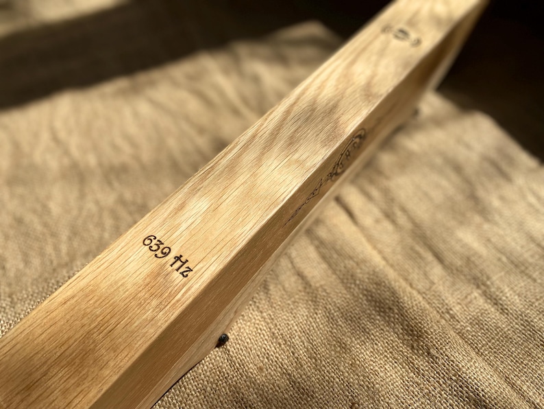 May include: A wooden tuning fork with the inscription "639 Hz" on the side. The tuning fork is resting on a brown fabric surface.
