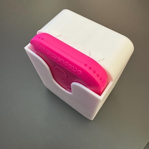May include: A white plastic holder with a pink octopus energy device inside. The device has the words "octopus energy" printed on it.