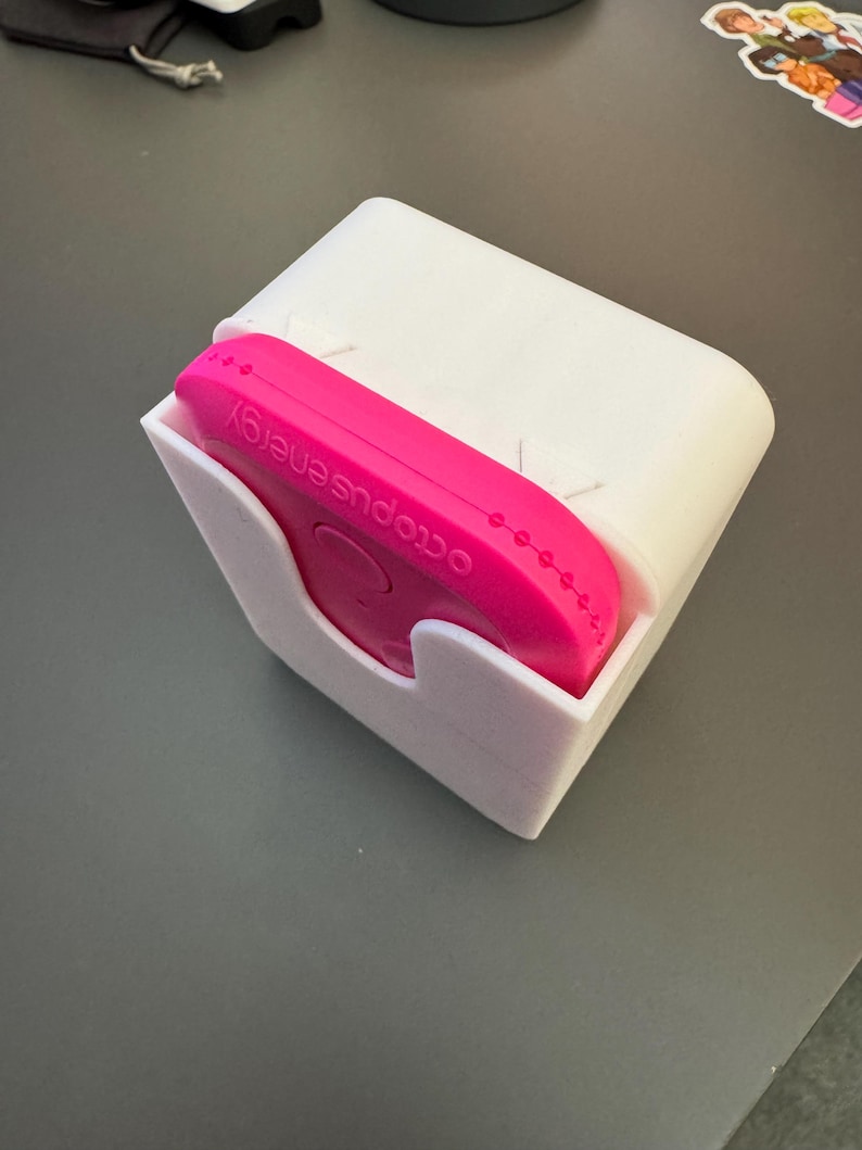 May include: A white plastic holder with a pink octopus energy device inside. The device has the words "octopus energy" printed on it.