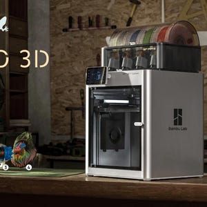 Puede incluir: Una impresora 3D plateada con el texto "GECKO 3D" y un logotipo de gecko. La impresora est&aacute; junto a varios objetos coloridos impresos en 3D. La impresora tiene una pantalla y un logotipo de Bambu Lab.