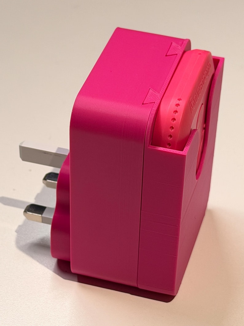 Puede incluir: Un adaptador el&eacute;ctrico rosa brillante con un enchufe de tres clavijas. El adaptador tiene una carcasa rectangular con una ranura para un dispositivo m&aacute;s peque&ntilde;o y redondeado. El dispositivo tambi&eacute;n es rosa y tiene la palabra "Galestron" impresa.