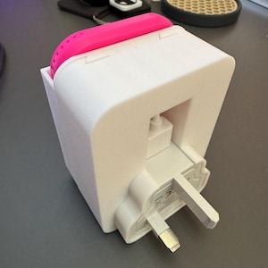 May include: A white electrical adapter with a pink silicone cover. The adapter has a three-prong plug and a small white button on the side.