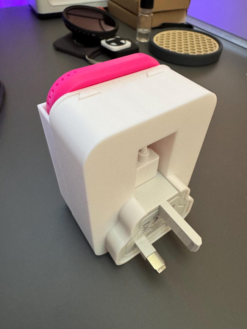 May include: A white electrical adapter with a pink silicone cover. The adapter has a three-prong plug and a small white button on the side.