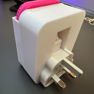 May include: White plastic adapter with a pink silicone cover. The adapter has a three-prong plug and is designed to fit into a standard wall outlet.