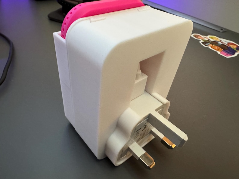 May include: White plastic adapter with a pink silicone cover. The adapter has a three-prong plug and is designed to fit into a standard wall outlet.