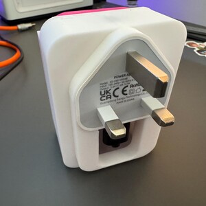 May include: White power adapter with a UK three-pin plug. The adapter has a label that reads "POWER ADAPTER" and includes the following information: Model: 10-2000000000, Input: 100-240V~ 50/60Hz 0.3A, Output: 5.0V 1.0A, RoHS, UK CA CE. The adapter is made in China.